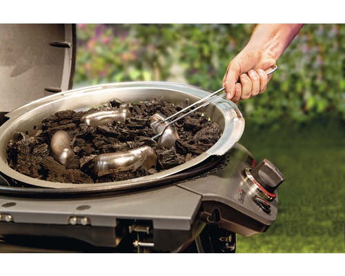 Offener Grill mit Holzkohle und Anzündkamin wird mit einer Grillzange befüllt.