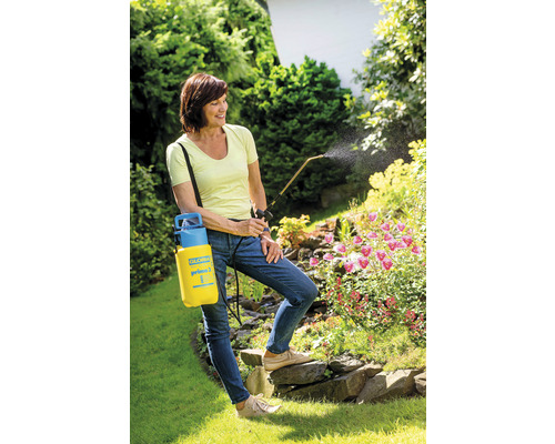 Frau verwendet eine gelbe Gartenspritze zur Pflanzenpflege im Garten.