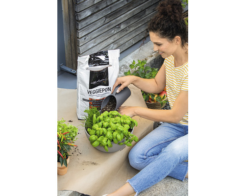 Frau befüllt einen Pflanztopf mit Kräutern und Gemüseerde Veggiepon.