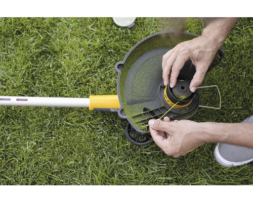 Person wechselt den Fadenkopf eines Rasentrimmers auf Rasen