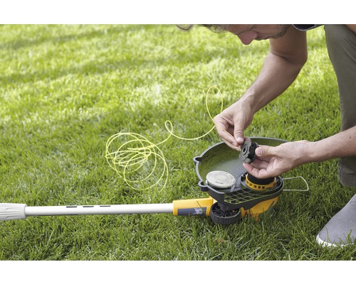 Mann fädelt Trimmerfaden in einen Rasentrimmer auf einer Wiese ein