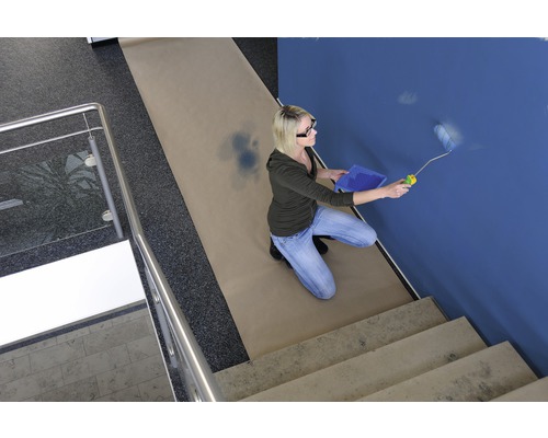 Frau streicht blaue Wand mit Farbroller, Abdeckpapier auf dem Boden