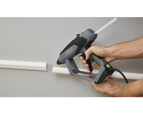Eine Person verwendet eine Heißklebepistole von Steinel, um eine Zierleiste an einer Wand zu befestigen.