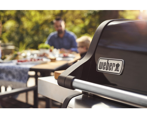 Weber Logo auf einem Grill mit Personen im Hintergrund