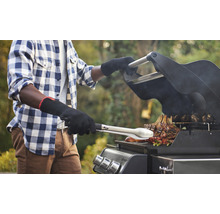 Mann grillt Fleisch mit Grillzange auf einem Grill.