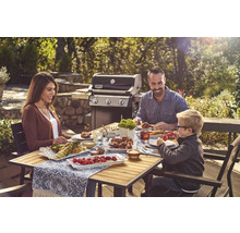 Familie grillt im Freien mit einem Gasgrill und genießt das Essen am Holztisch