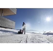 Eine Person bedient eine Schneefräse auf einer verschneiten Straße.
