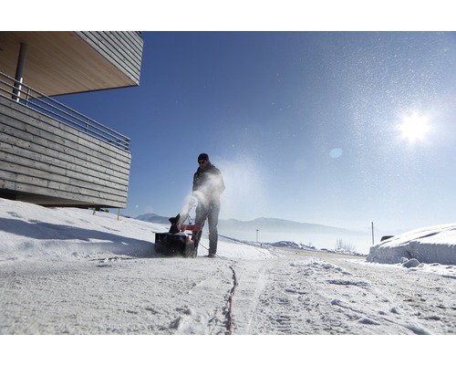 Eine Person bedient eine Schneefräse auf einer verschneiten Straße.