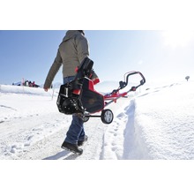 Eine Person trägt eine Schneefräse auf einem schneebedeckten Weg.