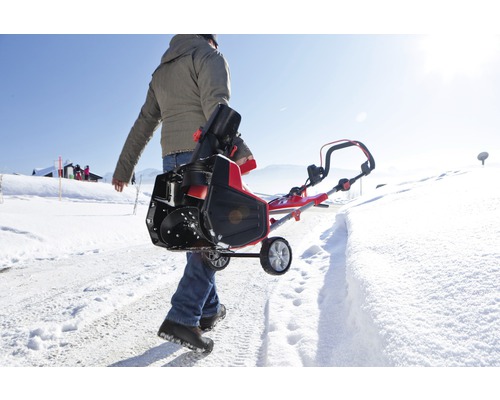 Eine Person trägt eine Schneefräse auf einem schneebedeckten Weg.