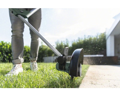 Eine Person schneidet mit einem Rasentrimmer Rasenkanten.