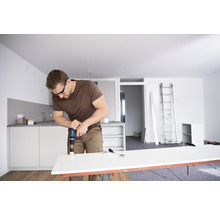 Mann bohrt Loch in Arbeitsplatte mit Bohrmaschine in heller Wohnung