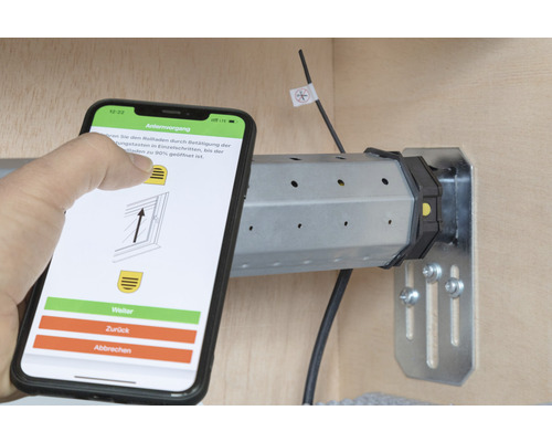Smartphone mit App zur Rollladensteuerung neben einem Rollladenmotor.