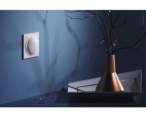 Intelligenter Lichtschalter an der Wand mit dekorativer Vase und Zweigen auf dem Tisch.