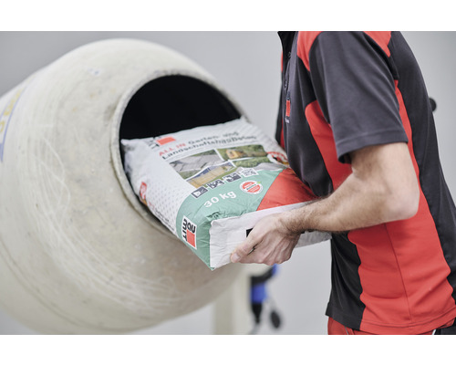 Eine Person schüttet einen Sack Garten- und Landschaftsbeton in einen Betonmischer