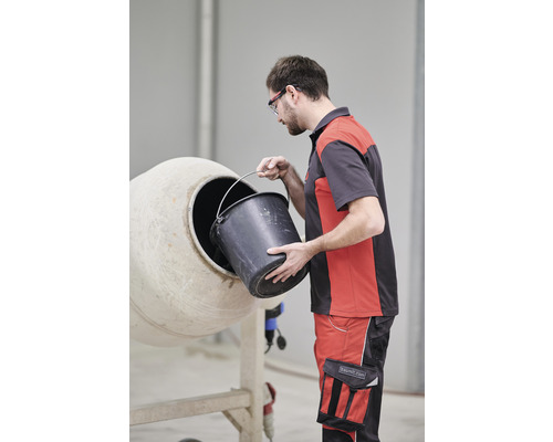 Mann gießt Inhalt eines Eimers in einen Betonmischer.