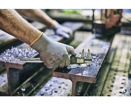 Eine Person misst mit einem Messschieber ein Stahlprofil, das mit Metallspänen bedeckt ist.