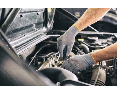 Ein Mann repariert mit Handschuhen und einem Schraubenzieher einen Automotor.