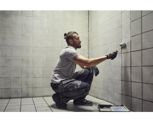 Mann streicht Fliesenwand mit Farbroller