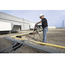 Ein Mann mit Schutzhelm sägt ein Rohr auf einem Dach mit einer Rohrsäge.
