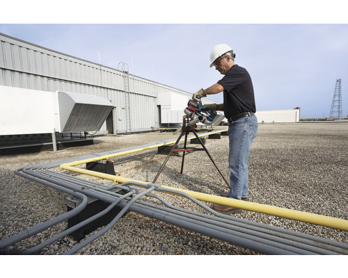 Ein Mann mit Schutzhelm sägt ein Rohr auf einem Dach mit einer Rohrsäge.
