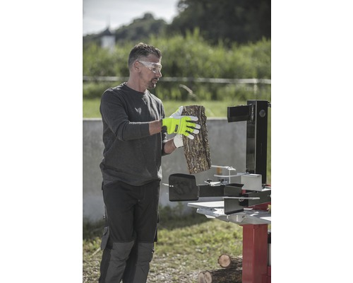 Mann mit Schutzbrille, Arbeitshandschuhen und Holzspalter bei der Holzbearbeitung