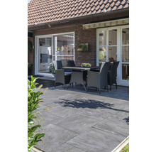 Außenbereich mit Steinfliesen, Gartentisch und Stühlen vor einem Haus.