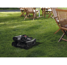 Rasenmähroboter auf Rasenfläche mit Gartenmöbeln im Hintergrund