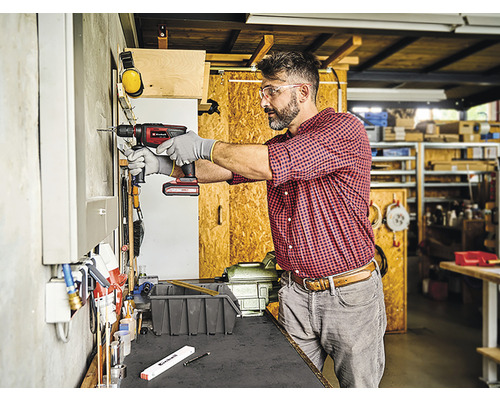 Handwerker bohrt mit einer Akku-Bohrmaschine ein Loch in eine Wand in einer Werkstatt.