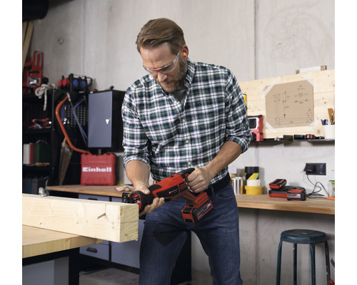 Mann sägt mit einer Akku-Säbelsäge ein Holzbrett in einer Werkstatt.