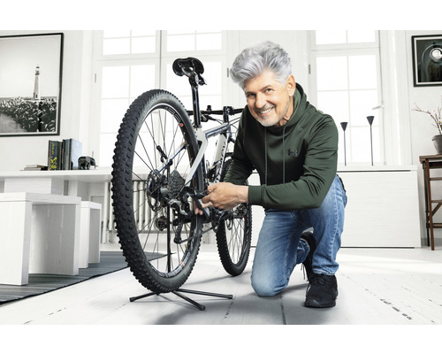 Mann repariert ein Fahrrad im hellen Raum.