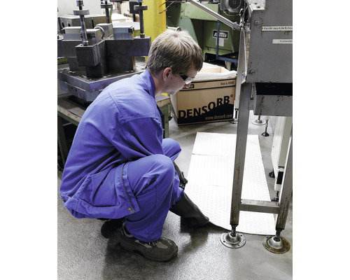 Ein Arbeiter in Arbeitskleidung legt Absorptionsmatten in einem Industriebereich aus.