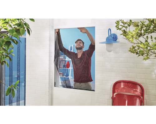 Mann montiert ein Insektenschutzgitter an einem Fenster.