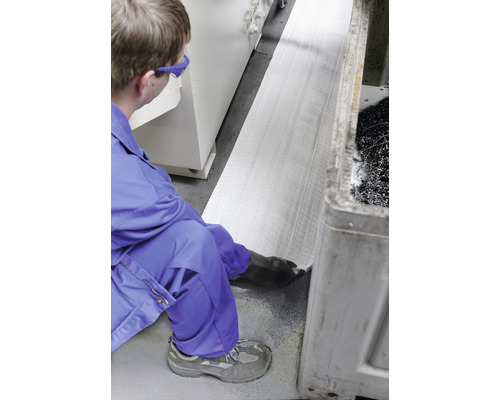 Eine Person in Arbeitskleidung legt eine Ölbindematte in einer Werkstatt aus.