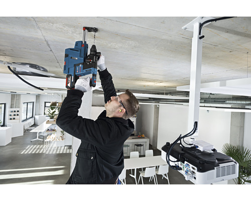 Ein Mann bohrt mit einer Bohrmaschine ein Loch in die Decke in einem Büro