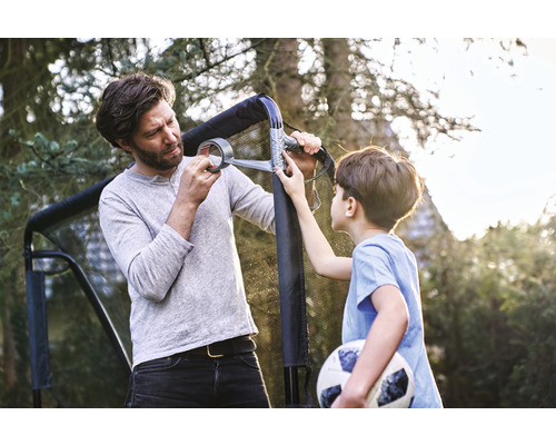 Ein Vater und sein Sohn reparieren mit Gewebeband ein Fußballtor im Garten.