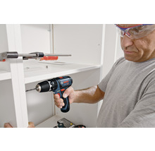 Ein Mann bohrt mit einem Akku-Bohrschrauber in ein weißes Regal