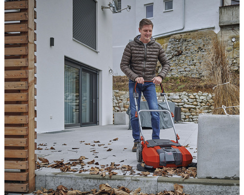 Ein Mann benutzt eine Kehrmaschine im Außenbereich, um Laub zu entfernen.