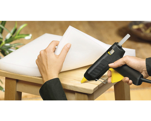 Eine Person befestigt Schaumstoff mit einer Heißklebepistole auf einem Holzstuhl.