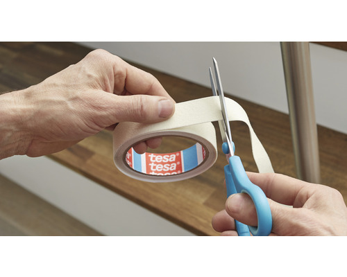 Eine Rolle Tesa-Kreppband wird mit einer Schere geschnitten.