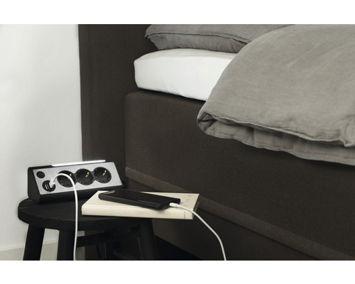 Mehrfachsteckdose mit USB-Anschlüssen und LED-Leuchte neben einem Bett auf einem Hocker