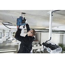 Ein Mann bohrt mit einer Schlagbohrmaschine ein Loch in die Decke in einem hellen Raum.