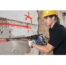 Ein Bauarbeiter mit Schutzhelm und Schutzbrille verwendet einen Bohrhammer an einer Wand