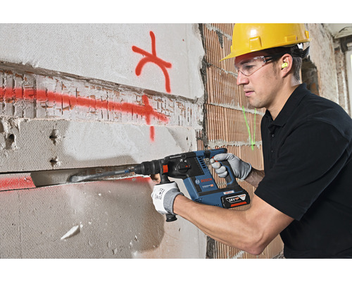 Ein Bauarbeiter mit Schutzhelm und Schutzbrille verwendet einen Bohrhammer an einer Wand