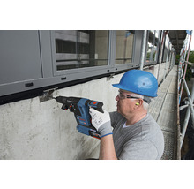 Mann bohrt mit einem Bohrhammer ein Loch in eine Wand auf einem Baugerüst