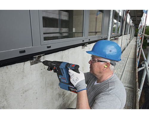 Mann bohrt mit einem Bohrhammer ein Loch in eine Wand auf einem Baugerüst