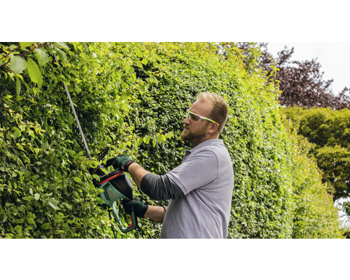 Mann schneidet Hecke mit Heckenschere im Garten.