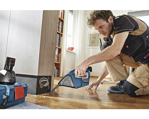 Ein Mann arbeitet mit einem Bohrhammer an einem Holzboden in einem Raum.