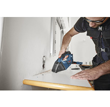 Handwerker säubert mit einem Akku-Handsauger eine Werkbank von Spänen.