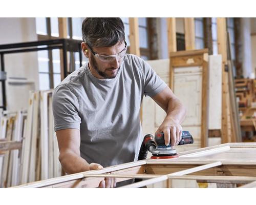 Ein Mann schleift Holz mit einem Exzenterschleifer in einer Werkstatt.